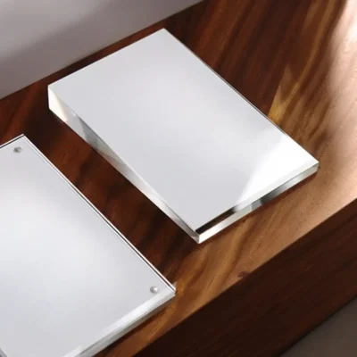 Une Porte-étiquette Magnétique Vertical incliné - A6 (100 x 150 mm) est posée sur une surface en bois, reflétant la lumière, tandis qu'un autre présentoir similaire est partiellement visible à proximité dans cette scène minimaliste et moderne.